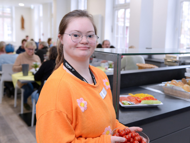 Eine Mitarbeiterin des Hotels hält eine Schale mit Tomaten in der Hand, die zum Frühstück gestellt werden. Sie lächelt in die Kamera.