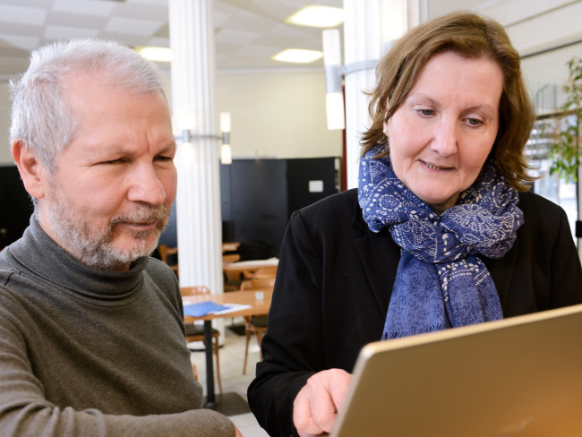 Eine Frau und ein Mann sitzen vor einem der Notebooks des Vringstreffs. Die Frau scheint dem Mann etwas auf dem Bildschirm zu zeigen.