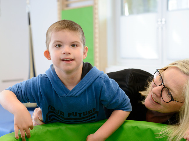 Lächelndes Kind in einem blauen Pullover spielt mit einer Erwachsenen im inklusiven Kinderzentrum