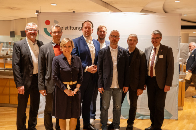 Acht Personen posieren für ein Gruppenfoto vor einem Banner der Sozialstiftung.