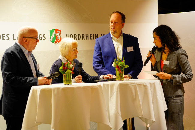 Vier Personen diskutieren an Stehtischen bei einer Veranstaltung im Landtag NRW.