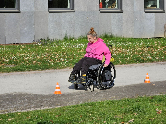 Frau im Rollstuhl meistert einen Parcours mit Hütchen im Freien, Förderung von Mobilität und Selbstständigkeit bei Mehrfachbehinderung