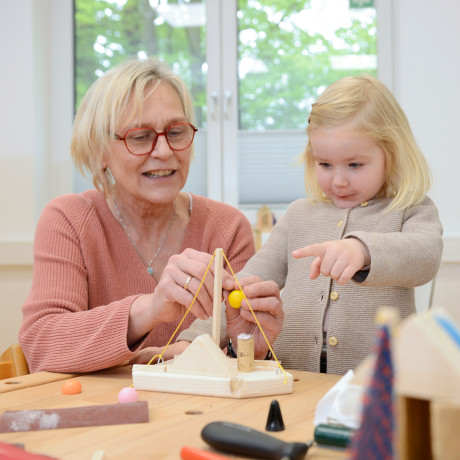 Ältere Frau und kleines Kind basteln zusammen an einem Tisch im inklusiven Kinderzentrum.